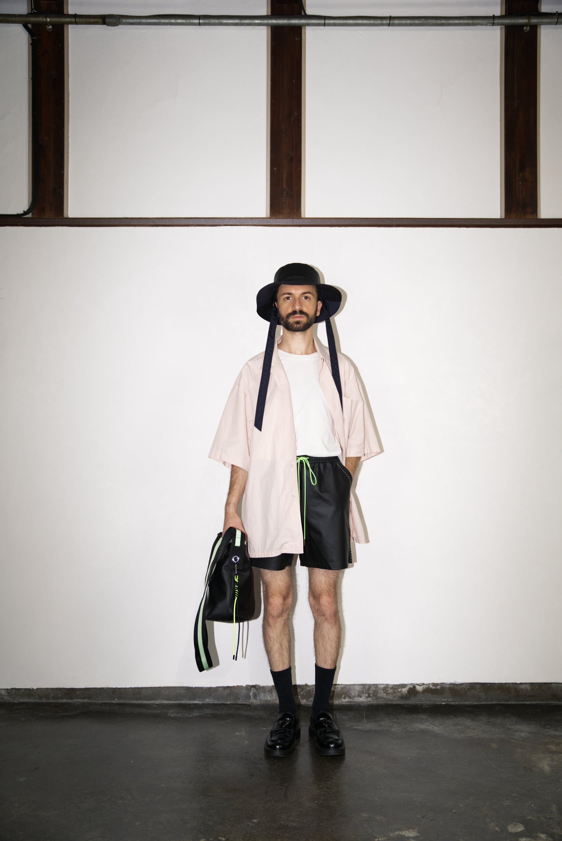 male model wearing the Hand-Stitched SCENE Cactus Leather Shorts in neon green with hat, bag and shirt