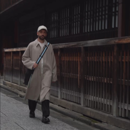 male model holding the Large Helmet Bag in Cactus Leather and walking down the street